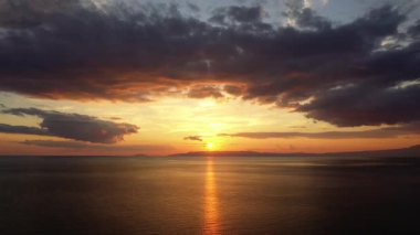 Sakin denizi yansıtan dramatik bulutlarla sersemletici bir gün batımı, dingin ve renkli bir ufuk yaratır..