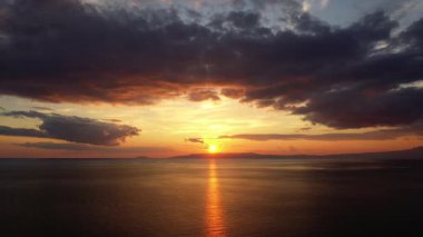 Sakin okyanus sularına yansıyan renkli bulutlarla canlı bir günbatımı. Huzurlu bir ufuk huzurlu ve ilham verici bir atmosfer yaratır..