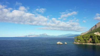 Scenic view of the Maratea coastline with clear blue sea, rocky shoreline, and lush green hills under a bright sky. Captured at Port de Porto in southern Italy.