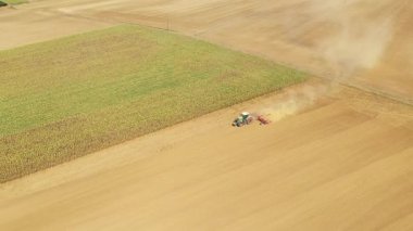 Bir traktörün havada yükselen tozla büyük, kuru bir tarlayı sürüşünün havadan görüntüsü. Kırsal tarım arazisi hasat mevsiminde yakalandı.