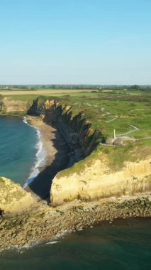 Fransa 'nın Pointe du Hoc kentindeki dramatik uçurumlar ve kayalık kıyı şeridi, açık mavi gökyüzü altında. Bereketli yeşil manzara ve uçurum boyunca görünen tarihi sığınaklar..