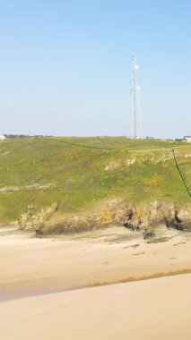 Geniş kumlu sahil ve yüksek iletişim anteni olan kayalık uçurum Cap de Carteret, Normandiya, Fransa 'da, açık mavi gökyüzünün altında.