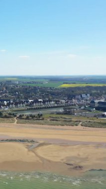 Juno Sahili 'nin manzaralı manzarası ve kıyı kasabası Courseulles-sur-Mer, Normandiya, kumlu kıyı şeridi, okyanus dalgaları ve açık mavi gökyüzünün altında kırsal alan..