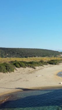 Yunanistan 'ın Gythio kenti yakınlarındaki turkuaz suları ve yemyeşil tepeleri olan sakin kumlu bir sahil, açık mavi bir gökyüzünün altında. Rahatlama, doğa ve Akdeniz manzaraları kavramları için ideal.