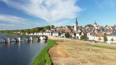Loire Nehri 'ni kaplayan ikonik taş köprüsü, tarihi binaları ve mavi gökyüzünün altındaki kilise kuleleriyle La Charite sur Loire' ın panoramik manzarası. Resimli ve huzurlu Fransız köyü sahnesi.