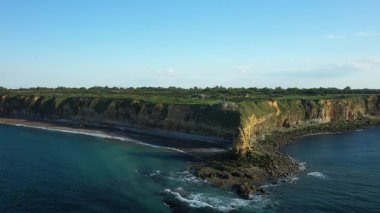 Pointe du Hoc, Normandiya, Fransa 'daki engebeli kayalıkların ve kıyı şeridinin geniş manzarası açık mavi bir gökyüzünün altında. Sahil manzarasında sarp kaya yüzeyleri ve denizin üzerindeki yeşil bitki örtüsü bulunur..