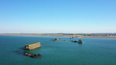 Yapay limandan, Gold Beach, Asnelles, Normandiya, Fransa açıklarındaki sakin mavi sulara uzanan beton yapıların havadan görüntüsü. Sahil şeridi ve temiz bir gökyüzünün altındaki köy..