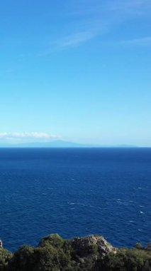 Derin mavi denizin geniş manzarası ve İtalya 'nın Capo di Conca kentindeki kayalık kıyı şeridinden berrak gökyüzü. Doğal bitki örtüsü ve uzak ufuk ile sakin deniz manzarası.