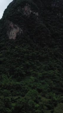 Bulutlu bir gökyüzünün altında Vang Vieng, Laos yakınlarındaki dramatik kireçtaşı dağlarını kaplayan yoğun tropikal orman. Yeşillik ve engebeli uçurumlar çarpıcı bir doğal manzara yaratır..