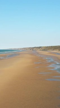 Fransa, Normandiya 'daki Omaha Sahili' nin geniş manzarası, altın kum, nazik dalgalar ve açık mavi bir gökyüzü. Sahil manzarası sakin ve sakin. Seyahat ve doğa temaları için ideal..