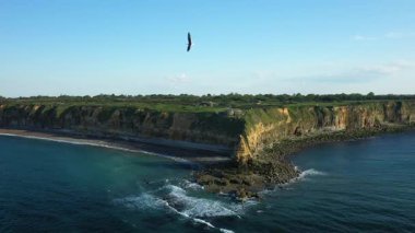 Fransa 'nın Pointe du Hoc kentindeki engebeli uçurumların ve kayalık kıyı şeridinin açık mavi gökyüzünün altındaki havadan görünüşü. Dramatik kıyı manzarası sarp kayalıkları ve sakin denizi barındırır..