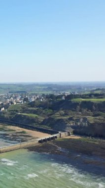 Kıyı kayalıklarının havadan görünüşü, bir dalgakıran ve açık mavi gökyüzü altında Fransa 'nın Normandiya' daki Port en Bessin köyü..
