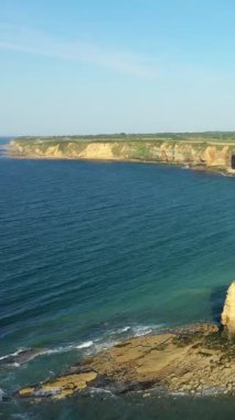 Normandiya 'nın Pointe du Hoc kentindeki engebeli uçurumların ve kayalık kıyı şeridinin manzarası berrak mavi bir gökyüzünün altında. Dramatik kıyı şeridi sakin denizle buluşup doğal bir manzara yaratıyor..