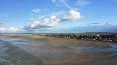 Ouistreham, Normandiya yakınlarındaki Sword Beach 'in geniş hava manzarası geniş kumlu kıyı şeridini ve dağınık bulutlu mavi bir gökyüzünün altındaki kıyı kasabasını gösteriyor..