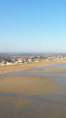 Sword Beach, Lion-sur-Mer, Normandiya 'da, açık mavi gökyüzünün altında gelgit havuzları ve kıyı evleri olan geniş kumlu sahil..