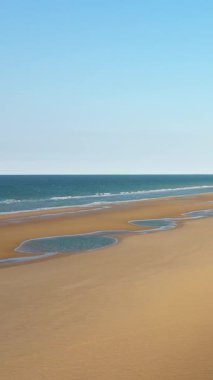 Fransa, Normandiya 'daki Omaha Sahili' nde açık mavi bir gökyüzünün altında yumuşak dalgalar ve gelgit havuzlarıyla geniş kumlu bir kıyı şeridi. Huzurlu kıyı manzarası seyahat ve doğa kavramları için ideal..