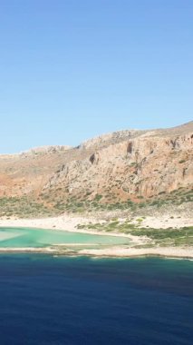 Girit 'in Balos Sahili' ndeki turkuaz gölün ve engebeli dağların açık mavi gökyüzünün altındaki hava manzarası. Huzurlu sahne, Akdeniz kıyılarının doğal güzelliklerini gözler önüne seriyor..