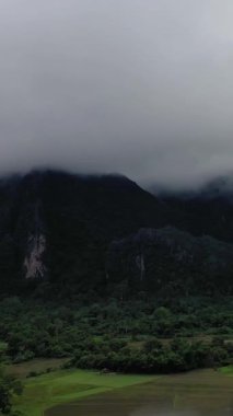 Bulutlu bir günde yoğun yeşil ormanlar ve Vang Vieng, Laos yakınlarındaki kırsal alanlar üzerinde dramatik sis kaplı dağlar yükselir..