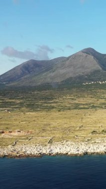 Yunanistan 'ın Cape Tenare kentinde berrak mavi suyu ve dramatik kayalık dağıyla engebeli bir kıyı şeridi manzarası. Manzara seyrek bitki örtüsü ve uzak, doğal bir atmosfere sahiptir..