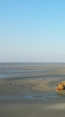 Fransa 'da Le Mont-Saint-Michel yakınlarındaki gelgit sularında açık mavi bir gökyüzünün altında gelgit düzlüklerinin ve kumlu sahillerin geniş manzarası..