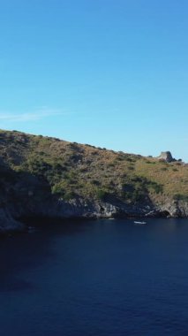 Açık mavi denizi olan kayalık bir kıyı şeridi manzarası ve parlak bir gökyüzünün altında İtalya 'nın Capo Palinuro kentindeki uçurumda tarihi bir gözlem kulesi..