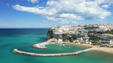 Peschici 'nin beyazlatılmış binalarının manzarası, turkuaz Adriyatik Denizi' nin üzerindeki bir uçuruma tünemiş, limanda bir marina ve limanda tekneler bulunuyordu. Parçalı bulutlu bir gökyüzünün altında resimli kıyı manzarası.