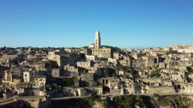 İtalya 'nın Matera kentindeki tarihi taş binalar ve katedralin panoramik manzarası, açık mavi gökyüzüyle doğal gün ışığıyla aydınlanıyor..