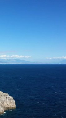 İtalya Capo di Conca 'daki kayalık sahil şeridi ile derin mavi denizin üzerinde açık mavi gökyüzü. Uzak dağları ve sakin okyanus sularıyla sakin Akdeniz manzarası.