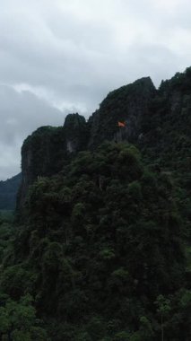 Vang Vieng, Laos yakınlarındaki bulutlu gökyüzünün altında dramatik yeşil karst dağı. Yoğun tropikal bitki örtüsüyle doğal manzara.