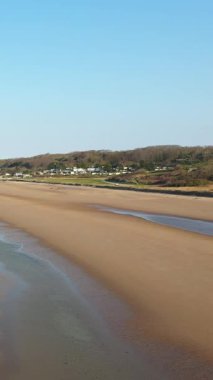 Fransa, Normandiya 'daki Omaha Sahili' nin geniş bir manzarası var. Açık mavi gökyüzü altında ıslak kum, gelgit havuzları ve uzak kıyı evleri var..