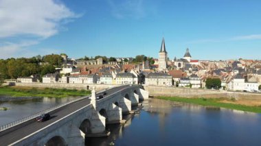 Loire Nehri 'ni geçen tarihi taş köprünün manzarası ve berrak mavi gökyüzünün altındaki La Charite sur Loire kasabasının manzarası. Geleneksel Fransız mimarisi ve kilise kuleleri gökyüzüne hakim..