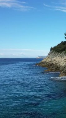 Açık mavi sular Yunanistan 'ın Karavostasi kentinde parlak bir gökyüzü altında engebeli kayalık bir kıyı şeridiyle buluşuyor. Huzurlu deniz manzarası seyahat ve doğa kavramları için idealdir.