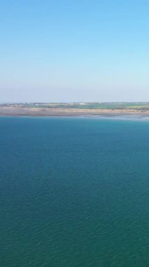 Fransa 'nın Normandiya, Asnelles yakınlarındaki Gold Beach' te kumlu kıyı şeridi ve uzak kırsal manzaralı sakin mavi deniz manzarası. Açık gökyüzü ve huzurlu kıyı manzarası.