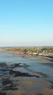 Arromanches-les-Bains, Normandiya, Fransa 'daki Arromanches-les-Bains' in havadan görünüşü, alçak gelgit sırasında açık gökyüzü ve arka planda kıyı uçurumları.