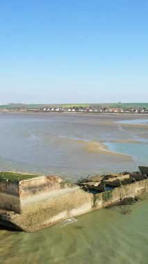 Asnelles, Normandiya 'daki Gold Beach' te, açık mavi gökyüzünün altında kıyı köyü olan yapay bir liman yapısının kalıntıları..