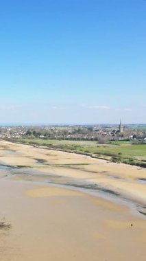 Kum, sığ su ve Fransa 'nın Normandiya kentindeki Bernieres-sur-Mer köyü ile birlikte açık mavi gökyüzü altında Juno Sahili' nin geniş manzarası..