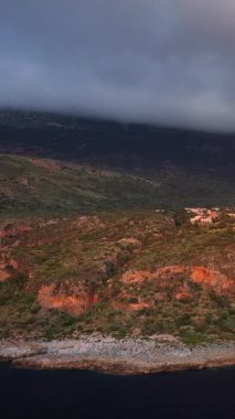 Dağılmış bitki örtüsüyle sarp kayalıklar, tepenin yamacına tünemiş küçük bir köy, dramatik alçak bulutların altında. Magne bölgesinde yakalandılar..