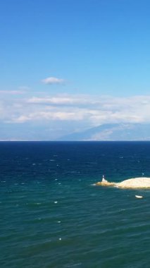 Scenic seascape featuring a stone breakwater and deep blue waters under a bright sky, with distant mountains visible on the horizon near Koroni, Greece.