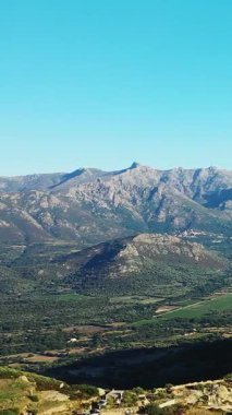 Scenic view of rugged mountains and lush green valleys under a clear blue sky in the Corsican countryside. Natural beauty and tranquility in rural Corsica.