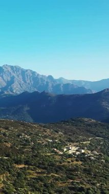 Scenic view of a mountainous landscape with a small rural village and lush greenery under a clear blue sky in Corsica, France.