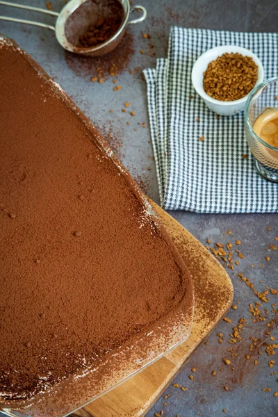 Traditional tiramisu cake in a glass pan on a wooden board served with a cup of coffee. Authentic gluten-free Italian layered dessert with ladyfinger biscuits, mascarpone cheese cream and cocoa powder