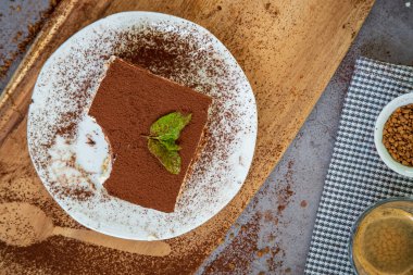 Arka planda bir fincan kahveyle geleneksel tiramisu pastası dilimi. Otantik glütensiz İtalyan katmanlı tatlı, ladyfinger bisküvileri ve kakao tozuyla süslenmiş mascarpone kremi. Üst görünüm