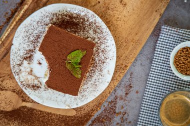 Arka planda bir fincan kahveyle geleneksel tiramisu pastası dilimi. Otantik glütensiz İtalyan katmanlı tatlı, ladyfinger bisküvileri ve kakao tozuyla süslenmiş mascarpone kremi. Üst görünüm