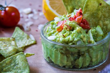 Taze ev yapımı avokado sosu, avokado aromalı, tortilla cipsi. Glütensiz geleneksel Meksika mutfağı ya da yemeği. Kahverengi kırsal kumaş üzerinde vişneli domates, soğan ve limon.