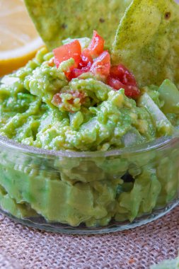 Taze ev yapımı guacamole sosu, yeşil avokado aromalı, tortilla cipsli. Glütensiz geleneksel Meksika mutfağı ya da yemeği. Arka planda vişneli domates, soğan ve limon var. Seçici odak