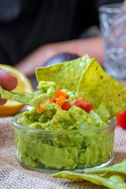El yapımı avokado soslu taze avokado sosu ve tortilla cipsi. Glütensiz geleneksel Meksika yemeği. Üstte vişneli domates, arkada soğan, limon ve patates kızartması..
