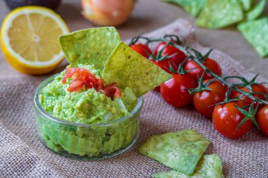 Taze ev yapımı avokado sosu, avokado aromalı, tortilla cipsi. Glütensiz geleneksel Meksika mutfağı, yemek. Çeri domatesleri ve arkaplanda koyu kahverengi kumaşla limon. Seçici odak