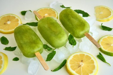 Ev yapımı dondurulmuş ve ferahlatıcı limonata buzlu buzlu dondurma ve buz küplü nane şekeri ve beyaz masada limon ve yeşil nane yaprakları.