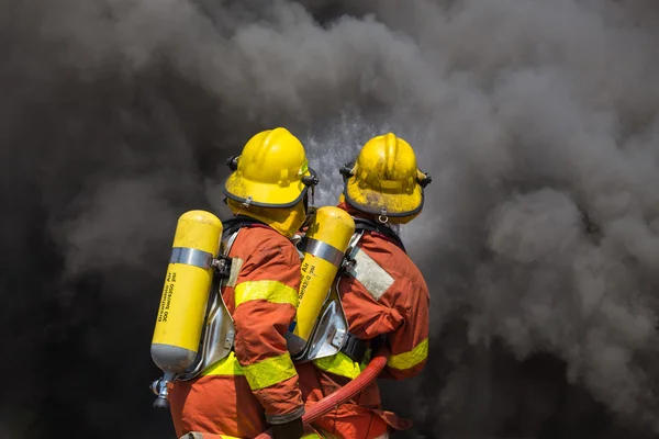 Two firefighter in fire fighting suit spraying water to fire and — Stock Photo, Image