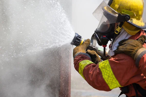 Bombero en traje de extinción de incendios rociando agua para fuego envolvente wi — Foto de Stock